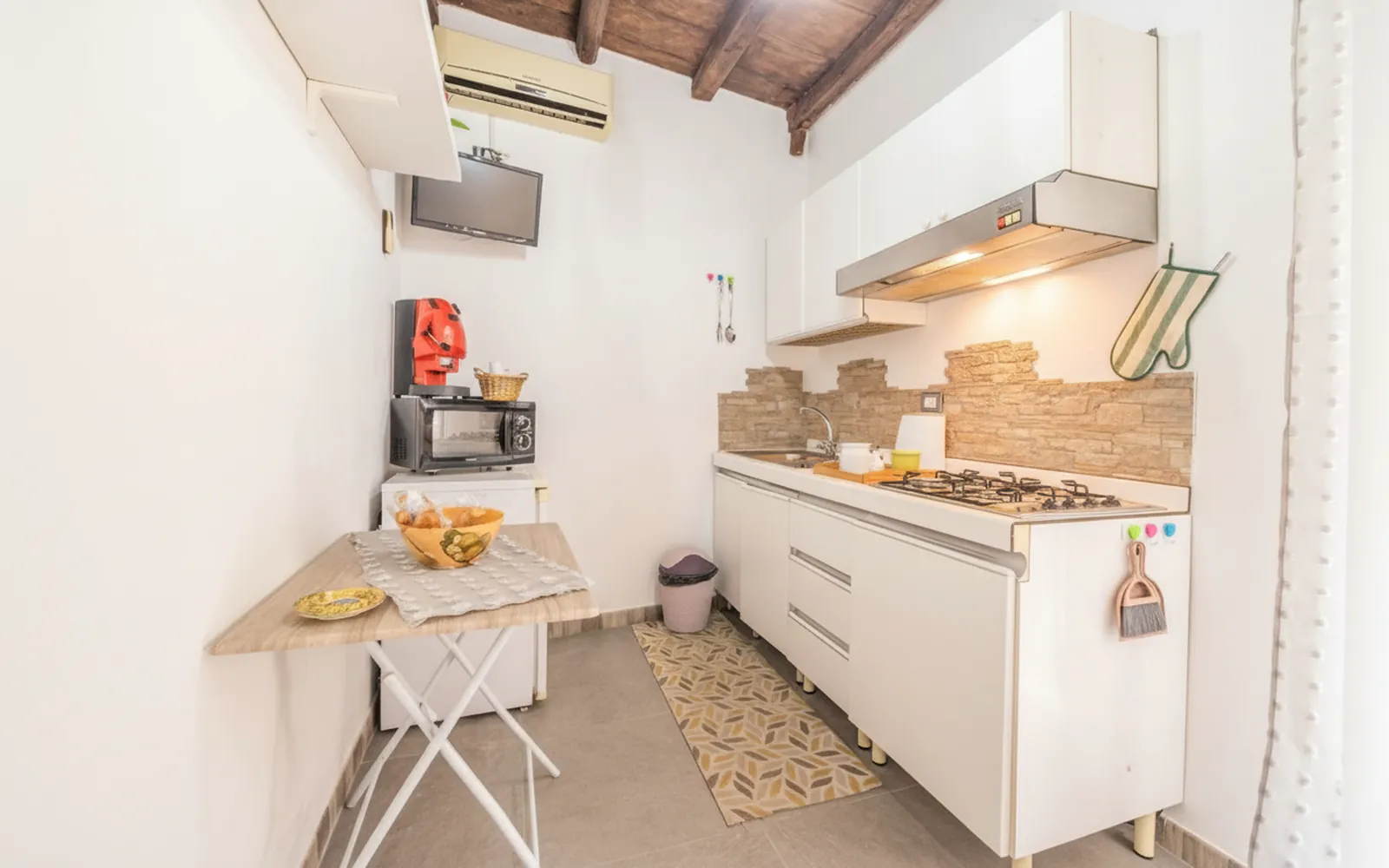 La cucina vista per intero, con il piano cottura, i pensili bianchi e il climatizzatore