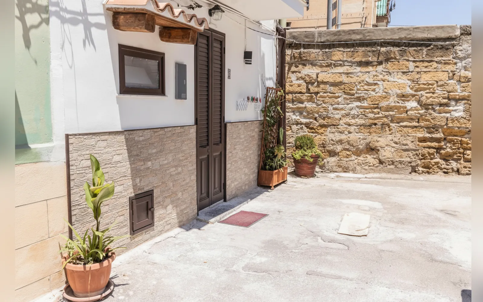 L’ingresso della casa con la porta in legno, le piante in vaso e il muro in pietra