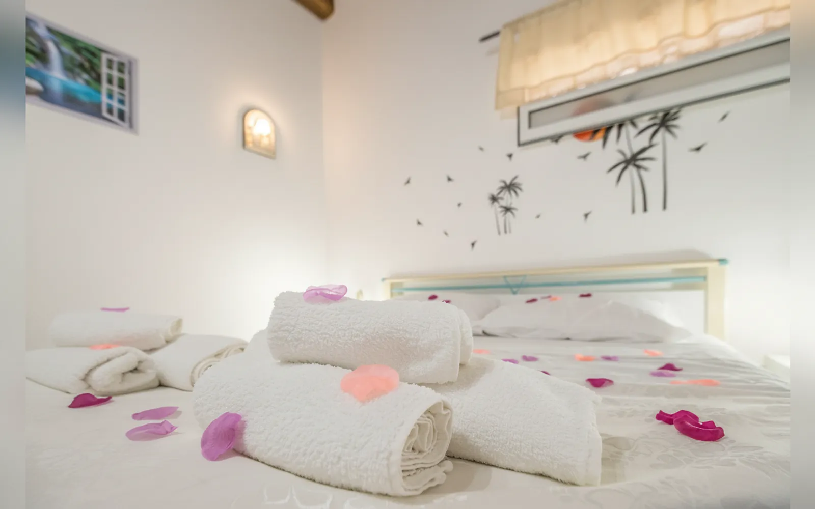 Gli asciugamani arrotolati sul letto matrimoniale, con la decorazione a palme sulla parete