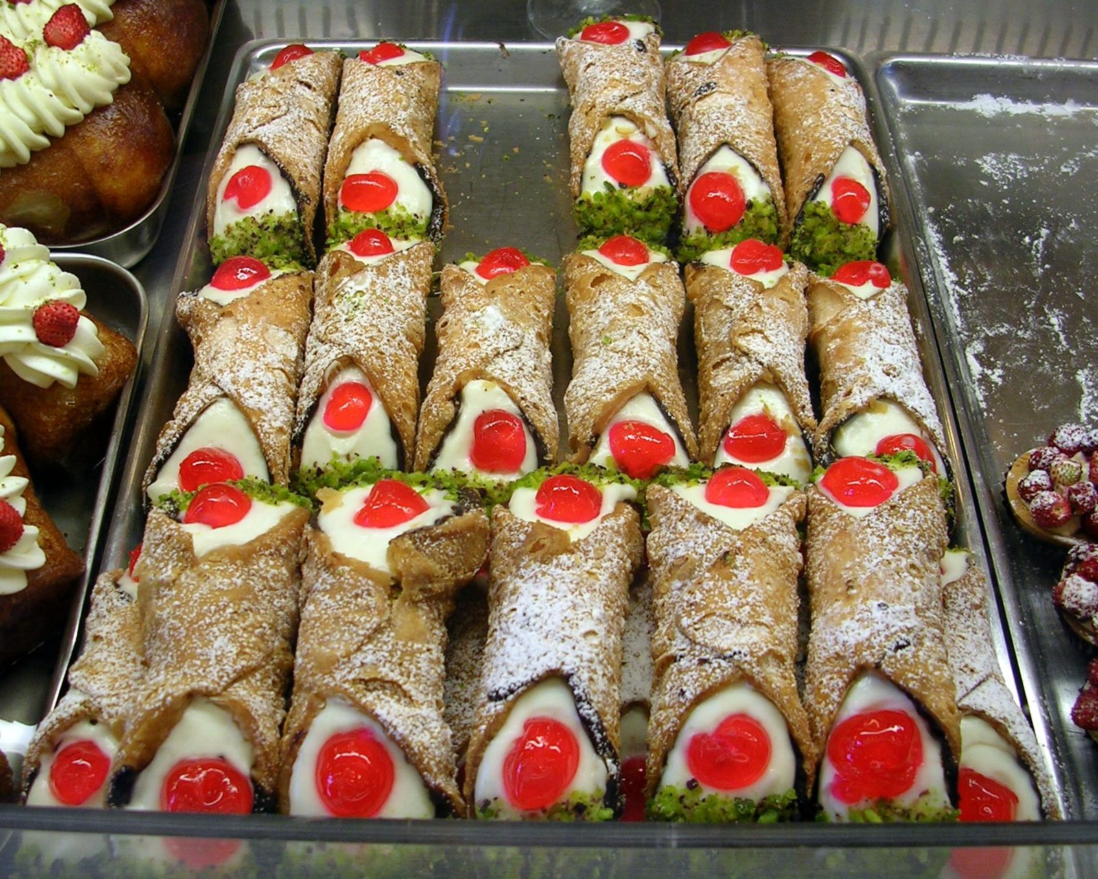 Un vassoio di cannoli siciliani ripieni di ricotta, decorati con ciliegie candite, granella di pistacchio e zucchero a velo