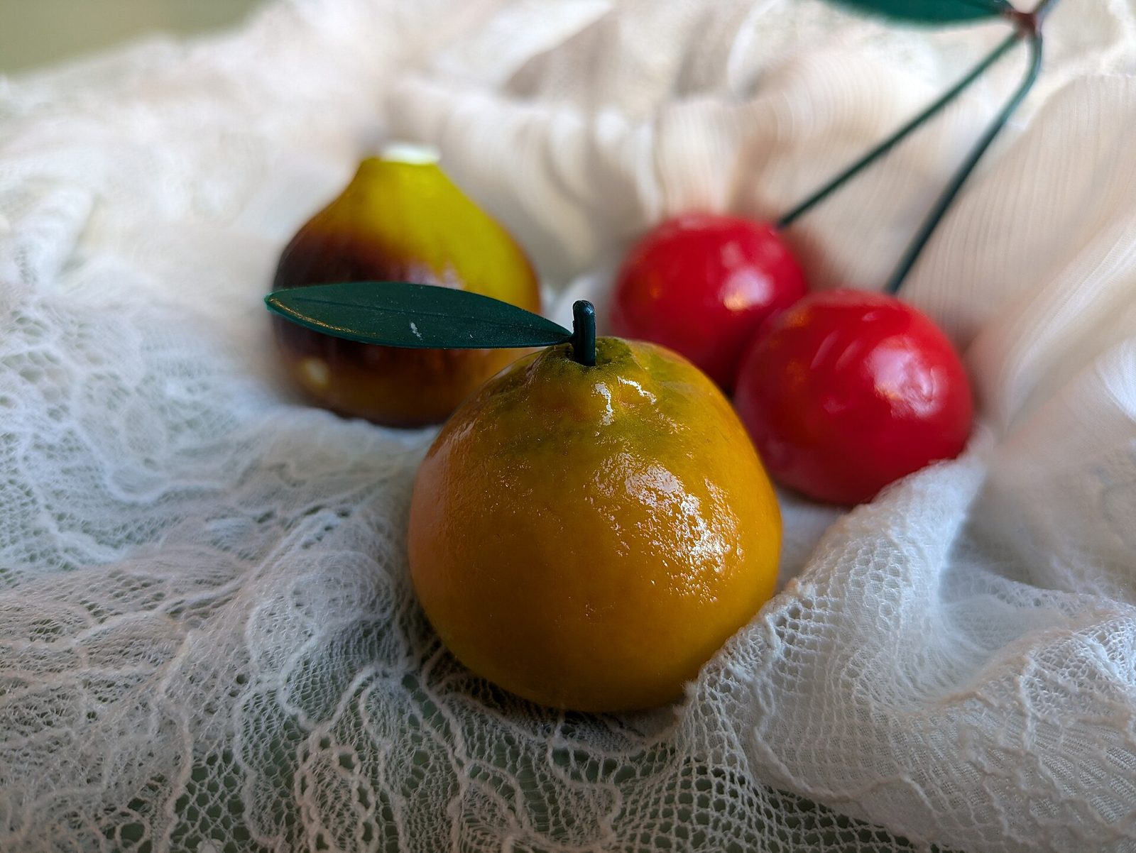 Frutta martorana di pasta di mandorle a forma di mandarino, pera e ciliegie, appoggiata su un panno di pizzo bianco