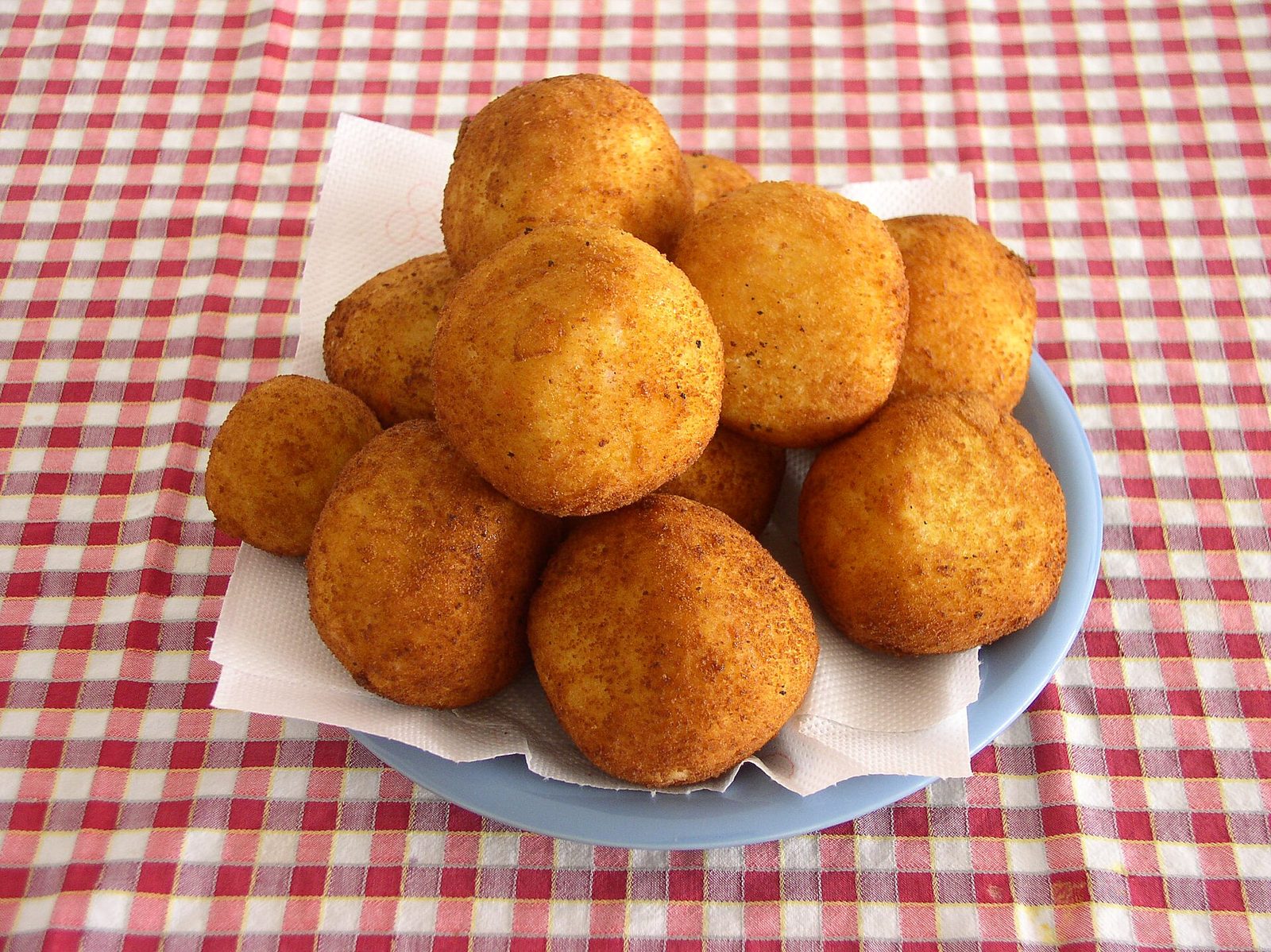 Un piatto di arancine tonde e dorate, all'uso palermitano, su una tovaglia a quadretti bianchi e rossi